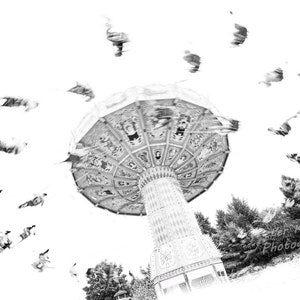 May include: Black and white photo of a carousel with people riding in the air. The carousel is in motion and the people are blurred. The photo is taken from below the carousel.