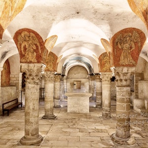 May include: A vaulted crypt with stone columns and arches. The walls are painted with murals of angels. The crypt is lit by a single window.