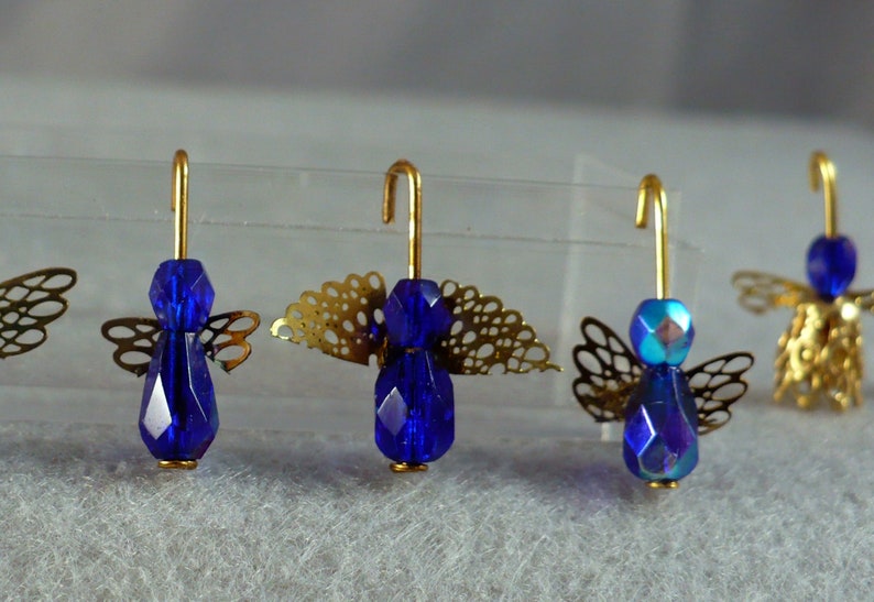 Op de afbeelding: Close-up van verschillende kleine engelornamenten. Elke engel heeft een facetgeslepen, diepblauwe kralenlichaam, een goudkleurige draadhalo en delicate goudkleurige filigraanvleugels. De engelen zijn in een rij gerangschikt, waarbij hun ingewikkelde details worden getoond.