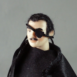 May include: A doll with a painted face, black hair, and a mustache. The doll wears a black eye patch and a black outfit. The doll's hair is styled with two long braids. The doll's skin is a light peach color.