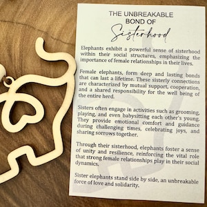 May include: A wooden elephant cutout necklace with a card that reads "The Unbreakable Bond of Sisterhood". The card describes the strong bonds of female elephants and how they support each other.