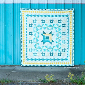 May include: A handmade quilt with a geometric design in shades of teal, yellow, and cream. The quilt features a central starburst pattern and a border of triangles. The background is a bright teal wall.