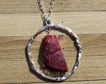 Large red and pink rough agate stone suspended inside from large silver circle on sparkly silver chain