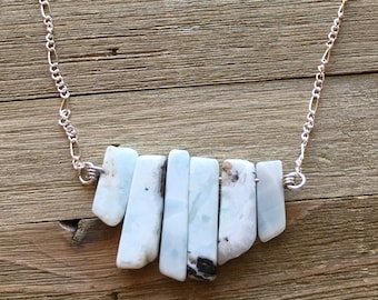 May include: A silver chain necklace with a pendant made of multiple light blue and white stones. The stones are arranged in a fan shape.