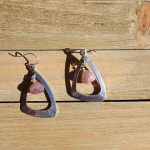 May include: A pair of silver earrings with a triangular shape and a dangling pink stone.