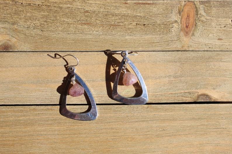 May include: A pair of silver earrings with a triangular shape and a dangling pink stone.