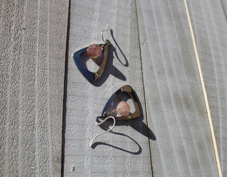 May include: A pair of silver triangle earrings with pink stone accents.