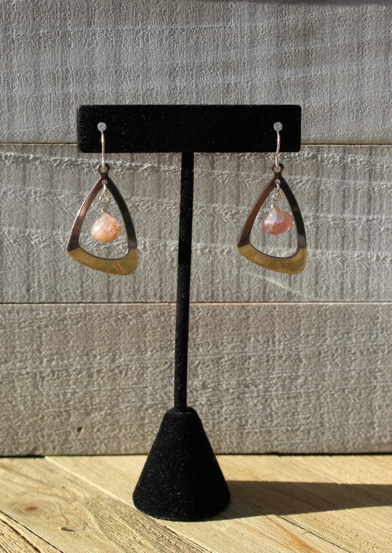 May include: A pair of silver earrings with a pink and white stone hanging from a triangle-shaped frame.