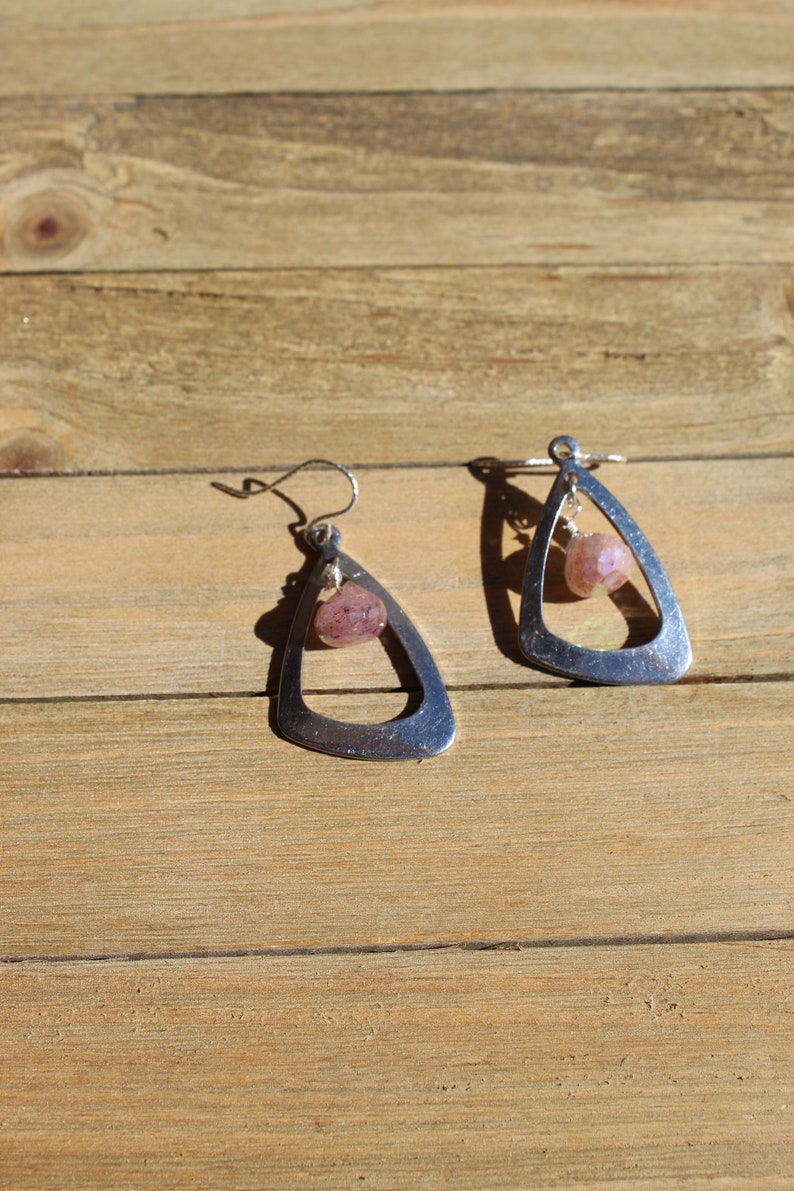 May include: A pair of silver dangle earrings with a pink gemstone hanging from each earring.