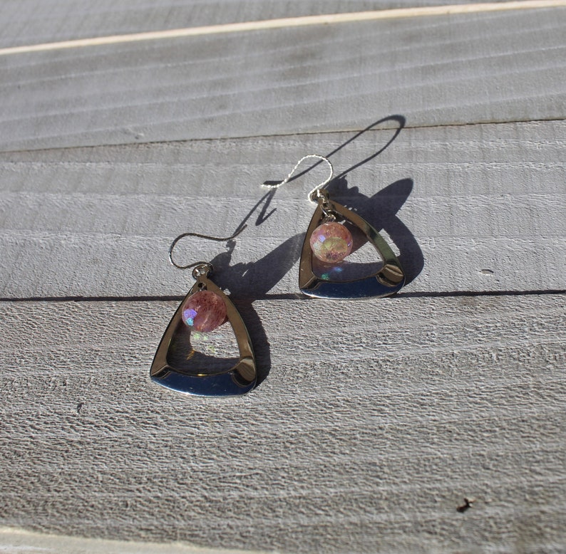 May include: A pair of silver triangle earrings with a pink iridescent stone in the center of each triangle.