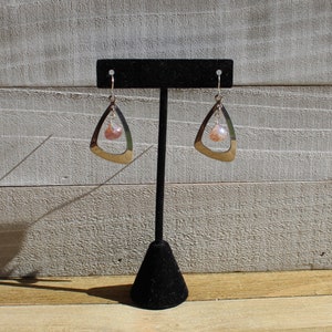 May include: A pair of silver earrings with a teardrop-shaped design and a pink gemstone dangle. The earrings are displayed on a black earring stand.