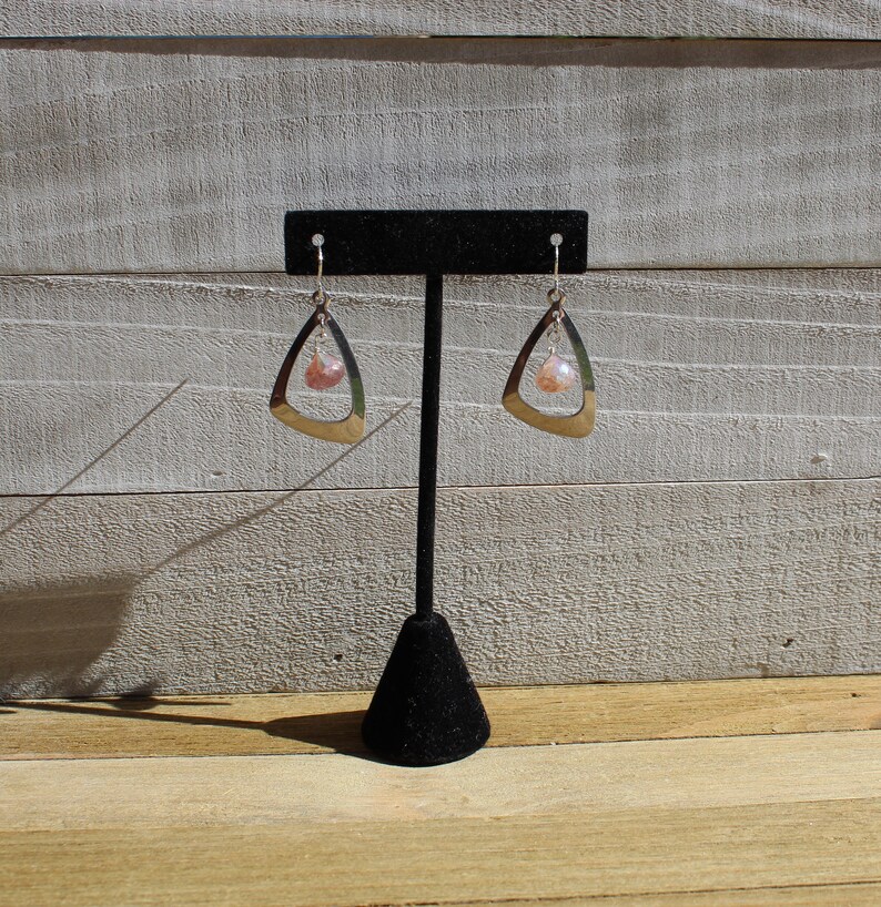 May include: A pair of silver dangle earrings with a pink and white gemstone hanging from each earring.