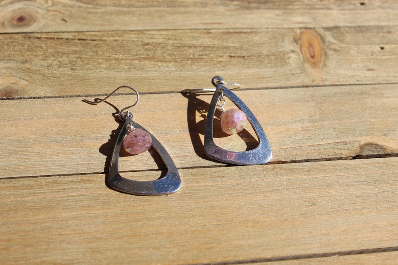 May include: A pair of silver dangle earrings with a pink and white glass bead hanging from each earring.