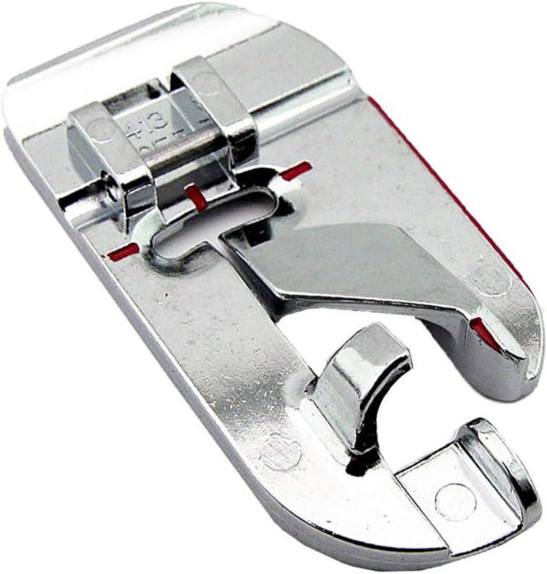 May include: A shiny, silver sewing machine foot with a curved design and a hinged top. The foot has red markings and is designed for sewing. The foot is made of metal and has a smooth, reflective surface.