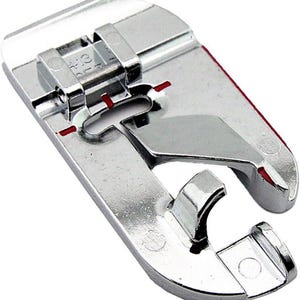 May include: A shiny, silver sewing machine foot with a curved design and a hinged top. The foot has red markings and is designed for sewing. The foot is made of metal and has a smooth, reflective surface.