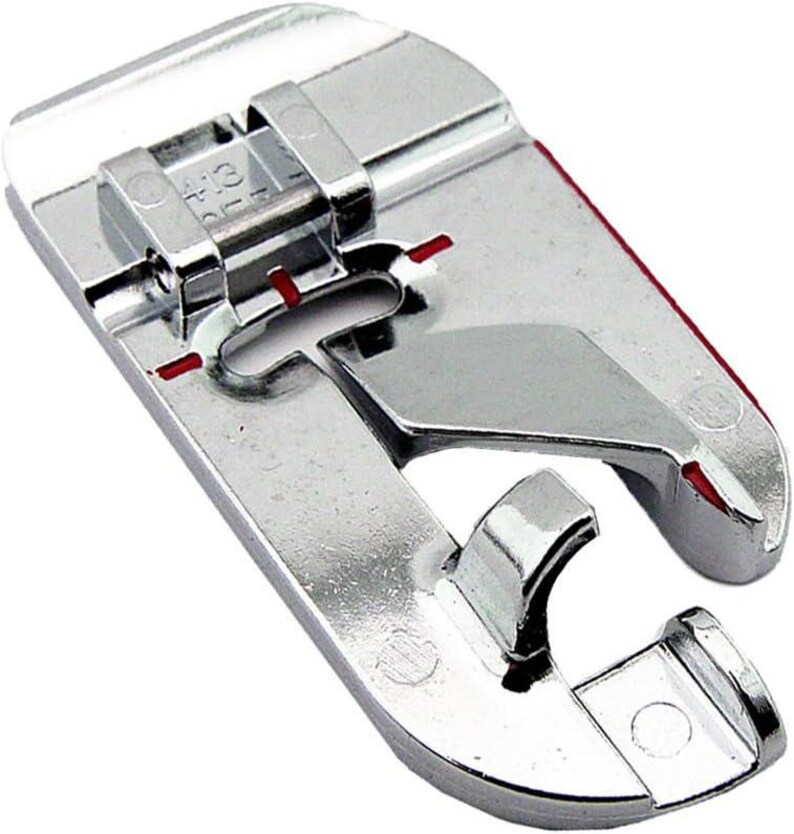 May include: A shiny, silver sewing machine foot with a curved design and a hinged top. The foot has red markings and is designed for sewing. The foot is made of metal and has a smooth, reflective surface.