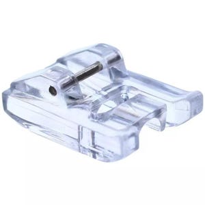 May include: A clear, transparent sewing machine presser foot. The foot is made of clear plastic and has a metal pin. The foot is designed to hold fabric in place while sewing. Sewing machine accessory.