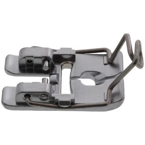 Puede incluir: Un prensatelas plateado para máquina de coser con un muelle de alambre curvado. El prensatelas tiene una base rectangular con una abertura central y dos piezas laterales. El muelle de alambre se extiende desde la base y se curva hacia arriba.