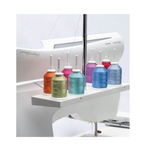 May include: A sewing machine with a white body and a selection of colorful thread spools. The spools are in shades of orange, green, pink, teal, purple, blue, and light blue. The machine has the text "Designer Diamond" and "Husqvarna Viking".