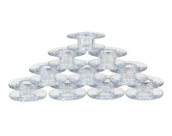 May include: A collection of clear plastic sewing machine bobbins arranged in a pyramid shape. Each bobbin has a circular flange on both ends and a central spool. The bobbins are transparent, allowing visibility of any thread used.
