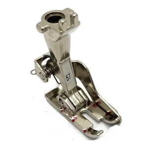 Puede incluir: Un prensatelas plateado para máquina de coser con el número 57 impreso. El prensatelas tiene un mecanismo de resorte y una base curva con marcas rojas. La parte superior tiene una abertura cilíndrica.