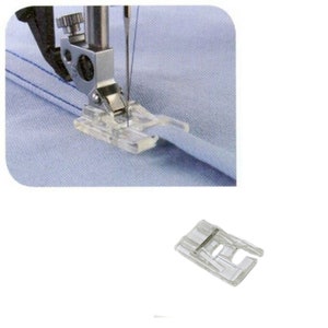 May include: Clear plastic sewing machine foot attached to a silver metal needle bar, sewing light blue fabric. A separate clear plastic sewing foot is shown below. Sewing machine parts.