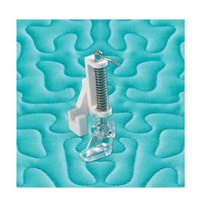 May include: A clear plastic quilting foot with a white bracket and a silver spring, designed for free-motion quilting. It is shown on a teal quilted fabric background.