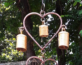May include: A wind chime made of metal hearts with gold bells hanging from each heart. The hearts are connected by a chain and the chime is hanging from a hook.