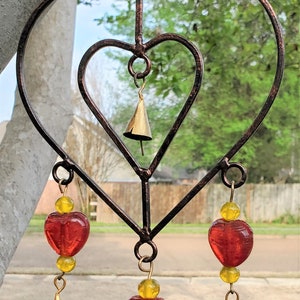 May include: A metal heart-shaped wind chime with three red glass hearts and four gold bells. The hearts are strung on a wire with yellow beads.