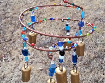 May include: A copper wire spiral wind chime with colorful glass beads and small gold bells. The chime is hanging from a copper chain.