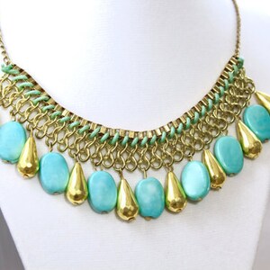 May include: A gold chain necklace with a green and gold chain design and turquoise teardrop-shaped beads.