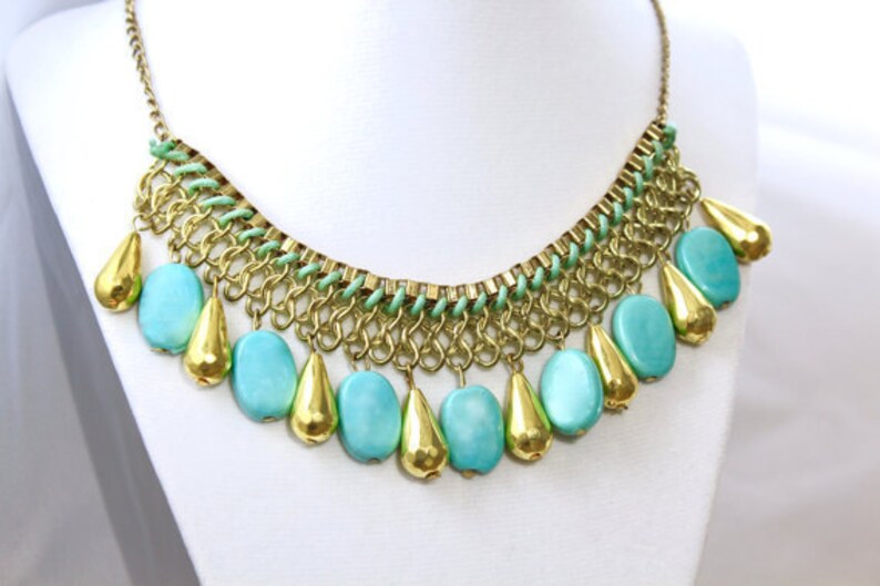 May include: A gold chain necklace with a green and gold chain design and turquoise teardrop-shaped beads.