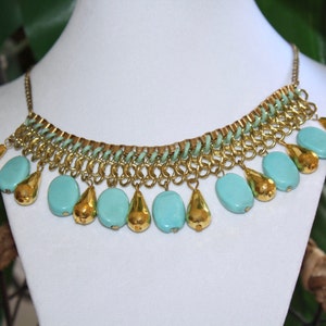 May include: A gold chain necklace with turquoise blue beads. The necklace has a delicate chain design and features a series of teardrop-shaped beads.