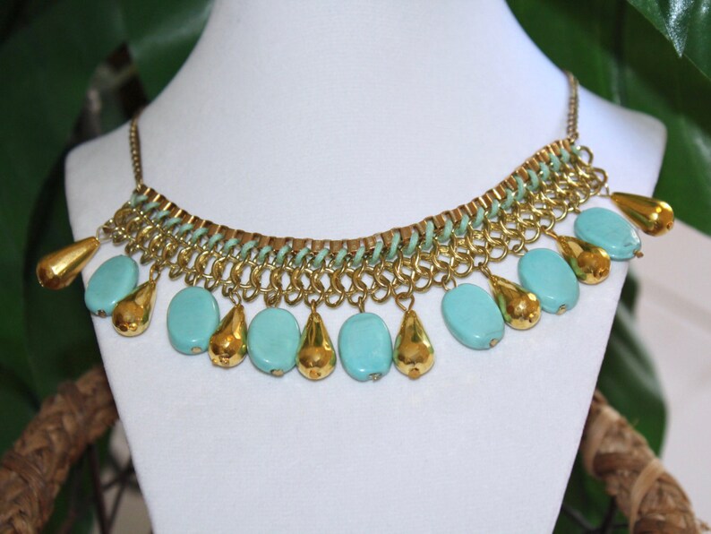 May include: A gold chain necklace with turquoise blue beads. The necklace has a delicate chain design and features a series of teardrop-shaped beads.