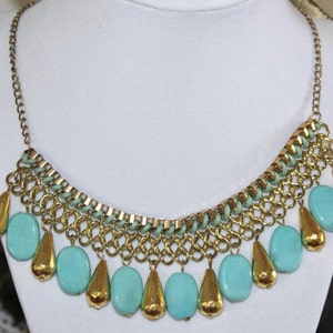 May include: A gold chain necklace with a turquoise and gold pendant. The pendant is made of multiple turquoise beads and gold chain links. The necklace is a statement piece and would be perfect for a night out.
