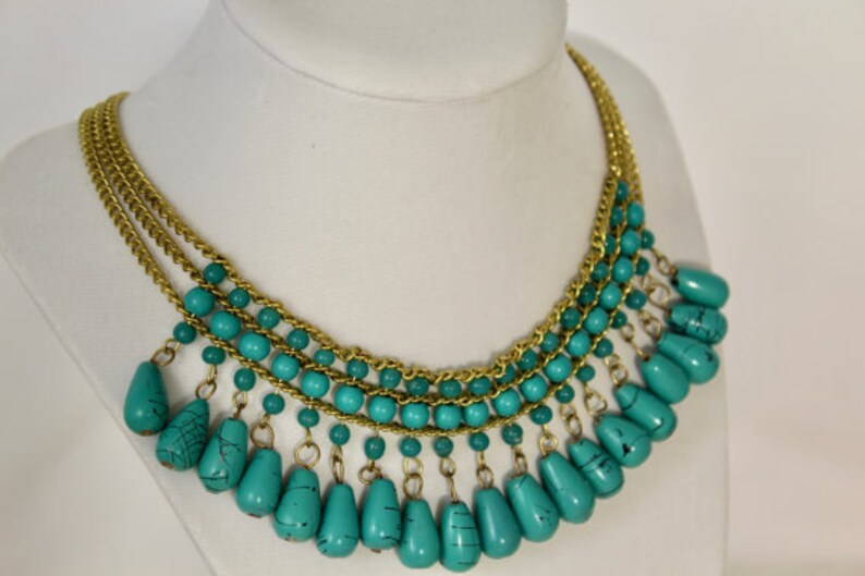 Pu&ograve; includere: Una collana turchese e oro con una catena a pi&ugrave; strati e perline a forma di goccia.