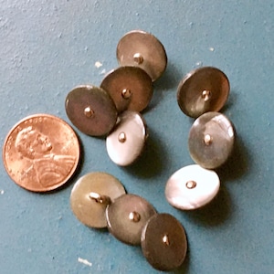 May include: A collection of vintage, iridescent, oval-shaped buttons with gold-colored shanks. The buttons are arranged on a blue surface next to a U.S. penny for size comparison. The buttons have a pearlescent sheen.