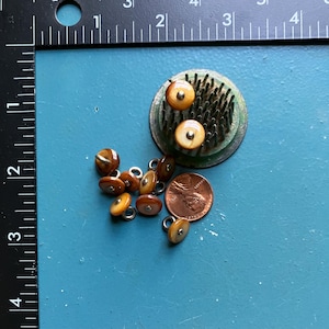 May include: A collection of vintage buttons in shades of brown and tan, with metal loops. A green and silver flower frog with three buttons is also present. A US penny is included for size reference.