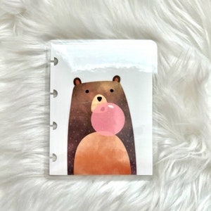 May include: A brown bear with a pink bubble in its mouth. The bear is illustrated in a cartoon style with a white background.