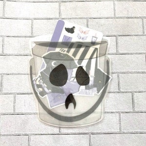 May include: A clear plastic bucket with a black and white striped design and a ghost face. The bucket is filled with various stickers, including bats, ghosts, and a cup of coffee.