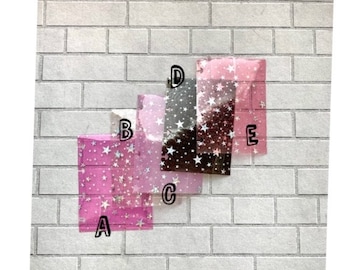 Può includere: Quattro fogli di plastica trasparente con un motivo a stella. I fogli sono rosa, nero e due tonalità di rosa. I fogli sono etichettati con le lettere A, B, C, D ed E.