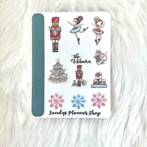 May include: A sheet of stickers featuring a Nutcracker, ballerinas, snowflakes, a Christmas tree, a mouse, and a gift box. The stickers are on a white background with a teal border. The text "The Nutcracker" and "Sandys Planner Shop" are printed on the sheet.
