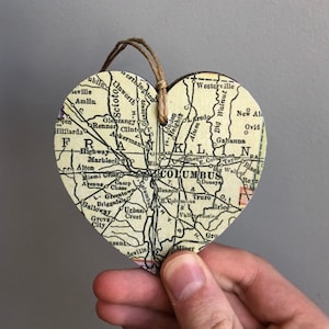 May include: A heart-shaped wooden ornament with a vintage map of Columbus, Ohio. The map features the city's major roads and landmarks, including the Scioto River and the Ohio Statehouse.
