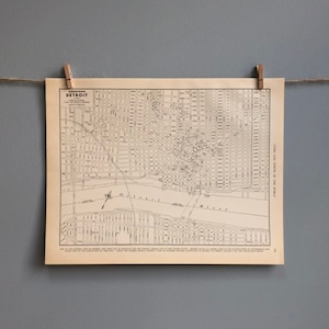 Może przedstawiać: Antyczna mapa Detroit, Michigan, wydrukowana na kremowym papierze. Mapa przedstawia ulice i punkty orientacyjne miasta, w tym rzekę Detroit. Mapa nosi tytuł "Commerce Detroit" i pochodzi z 1917 roku.