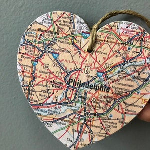 May include: A heart-shaped map of Philadelphia, Pennsylvania, with surrounding towns and cities. The map is printed on a light brown background with black and red text. The map is attached to a string.