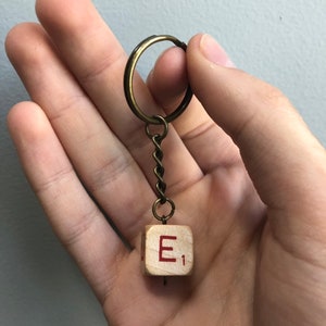 May include: A wooden keychain with a letter E and the number 1 on it. The keychain is attached to a gold-colored chain and ring.