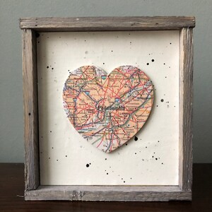 May include: A framed heart-shaped map of Philadelphia, Pennsylvania, with black paint splatters on a white background. The frame is made of weathered wood.