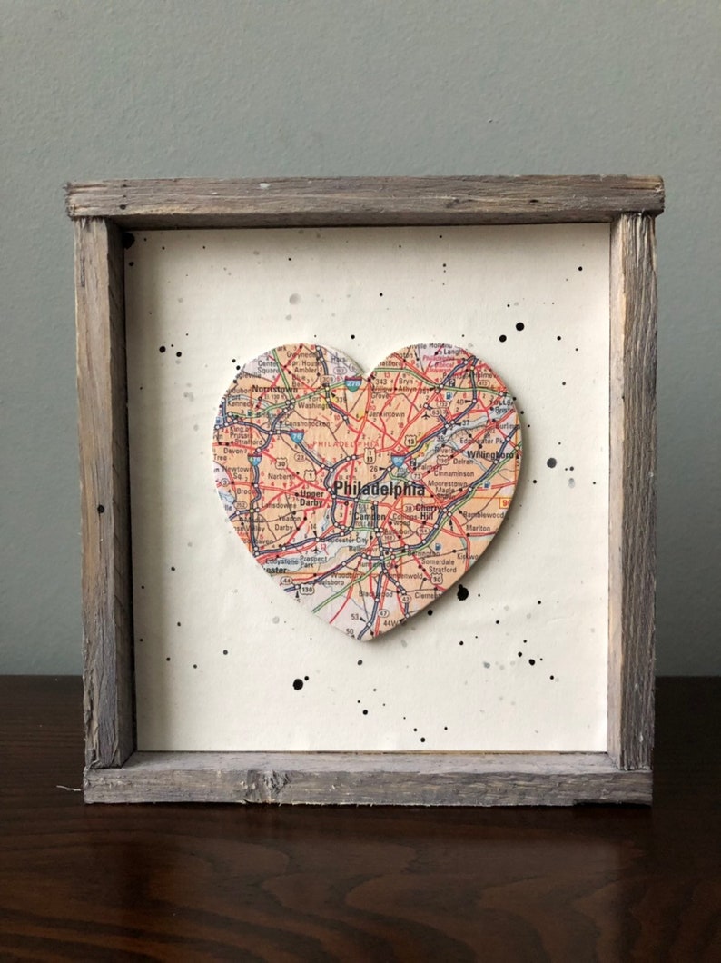 May include: A framed heart-shaped map of Philadelphia, Pennsylvania, with black paint splatters on a white background. The frame is made of weathered wood.