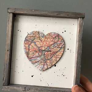 May include: A framed heart-shaped map of Philadelphia, Pennsylvania. The map is in a rustic wooden frame with a white background and black splatter paint.