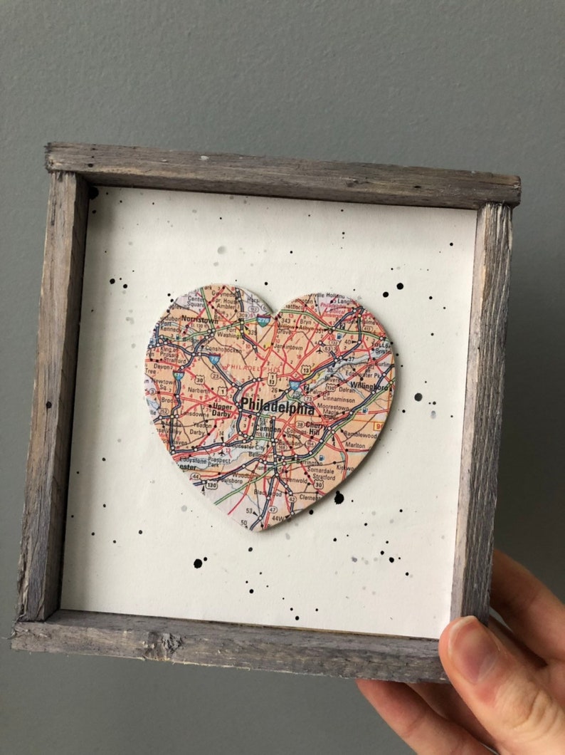 May include: A framed heart-shaped map of Philadelphia, Pennsylvania. The map is in a rustic wooden frame with a white background and black splatter paint.